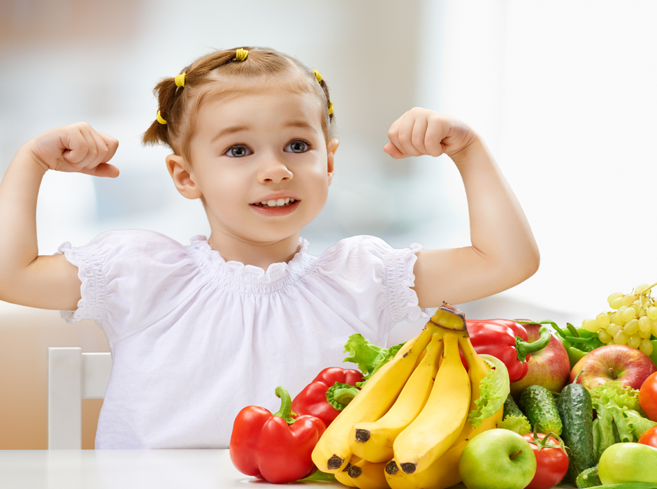 girl showing muscles in front of fruits and vegetables