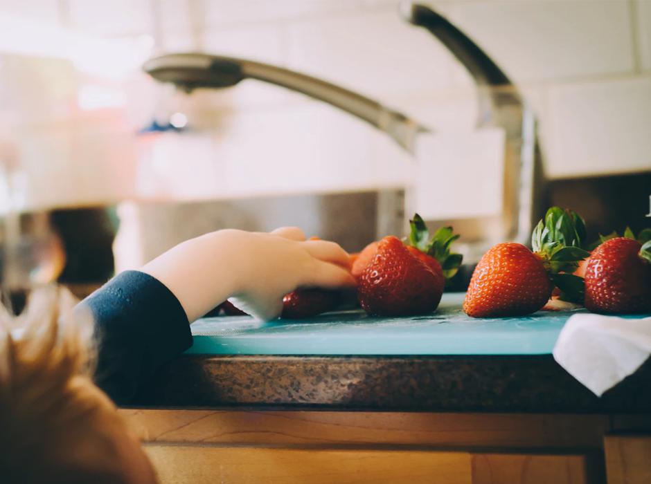 small hand grabbing strawberries on a counter