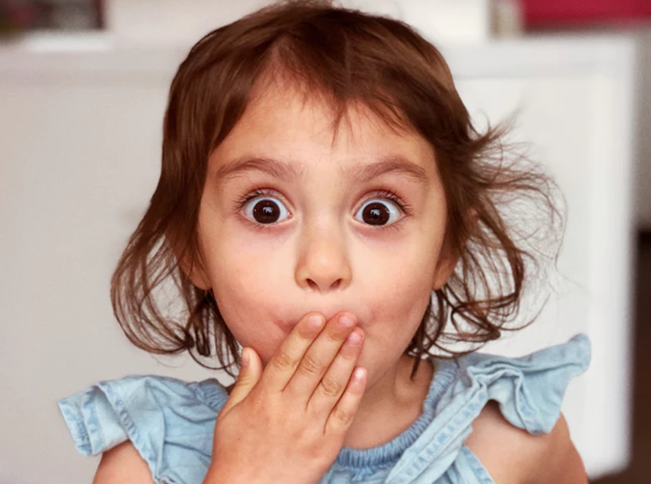 adorable girl with her hand over her mouth like she is surprised